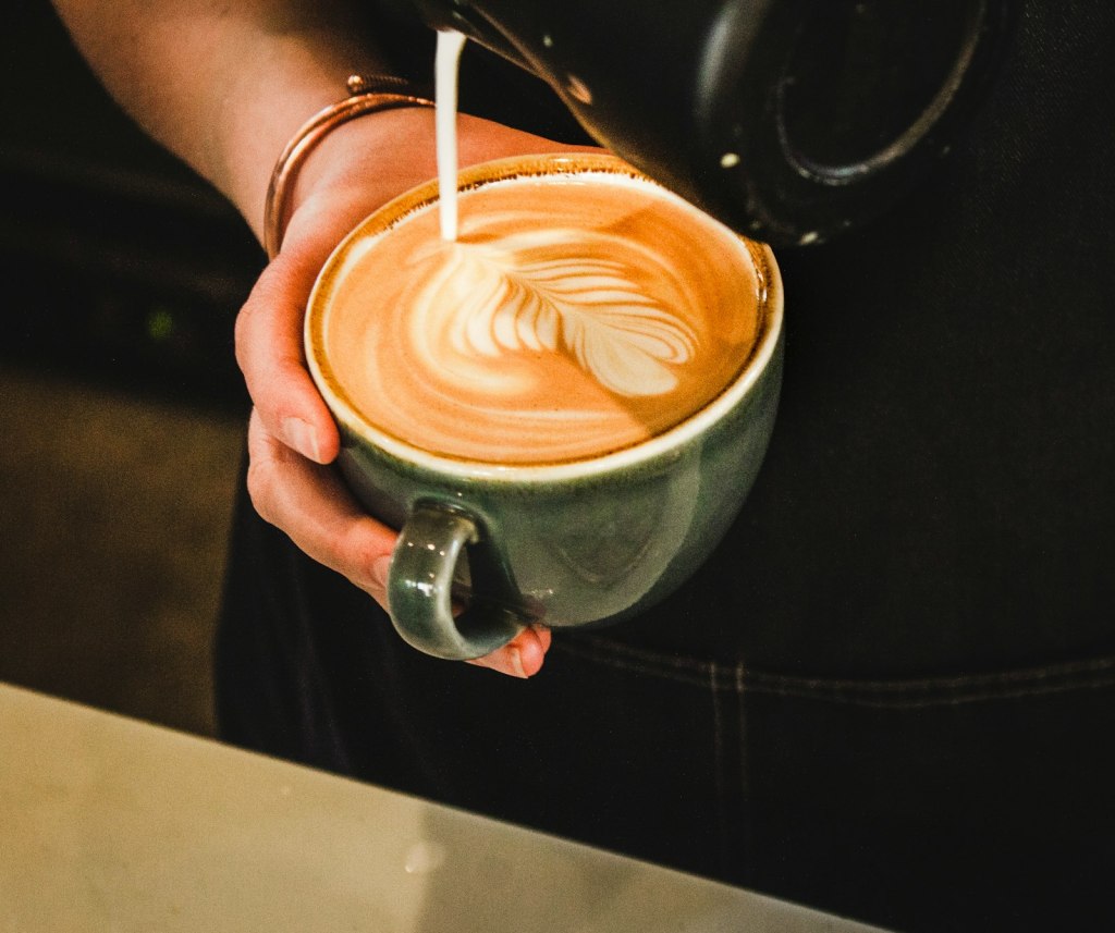 A barista pouring latte art into a green cup