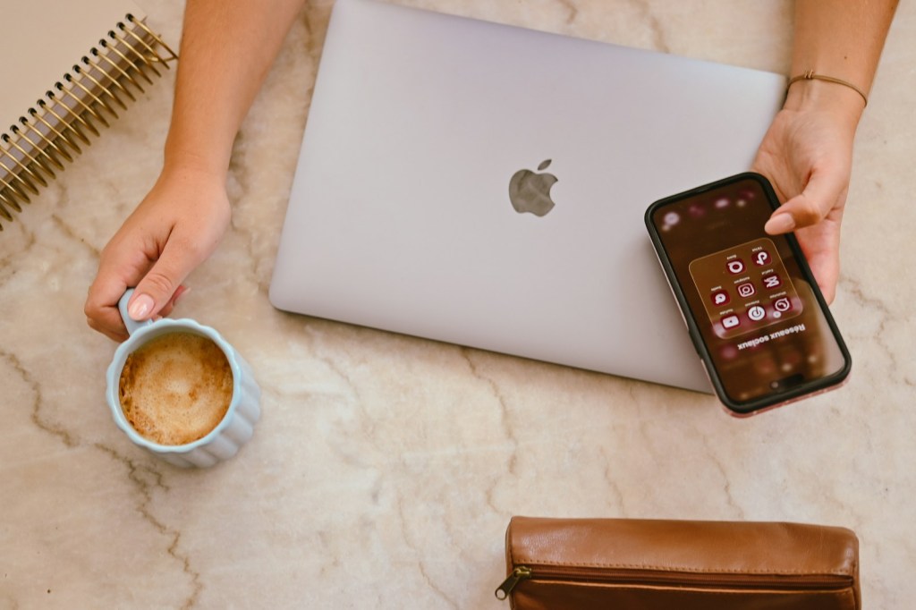 Person holding a coffee mug and a smartphone showing social media icons.