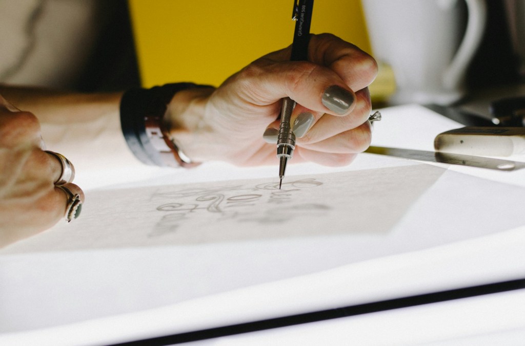 Hand sketching a logo design on tracing paper with a pencil.