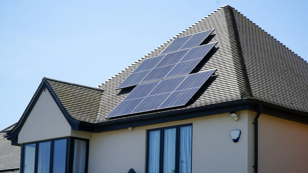 Rows of solar panels fitted to the roof of a house under a blue sky