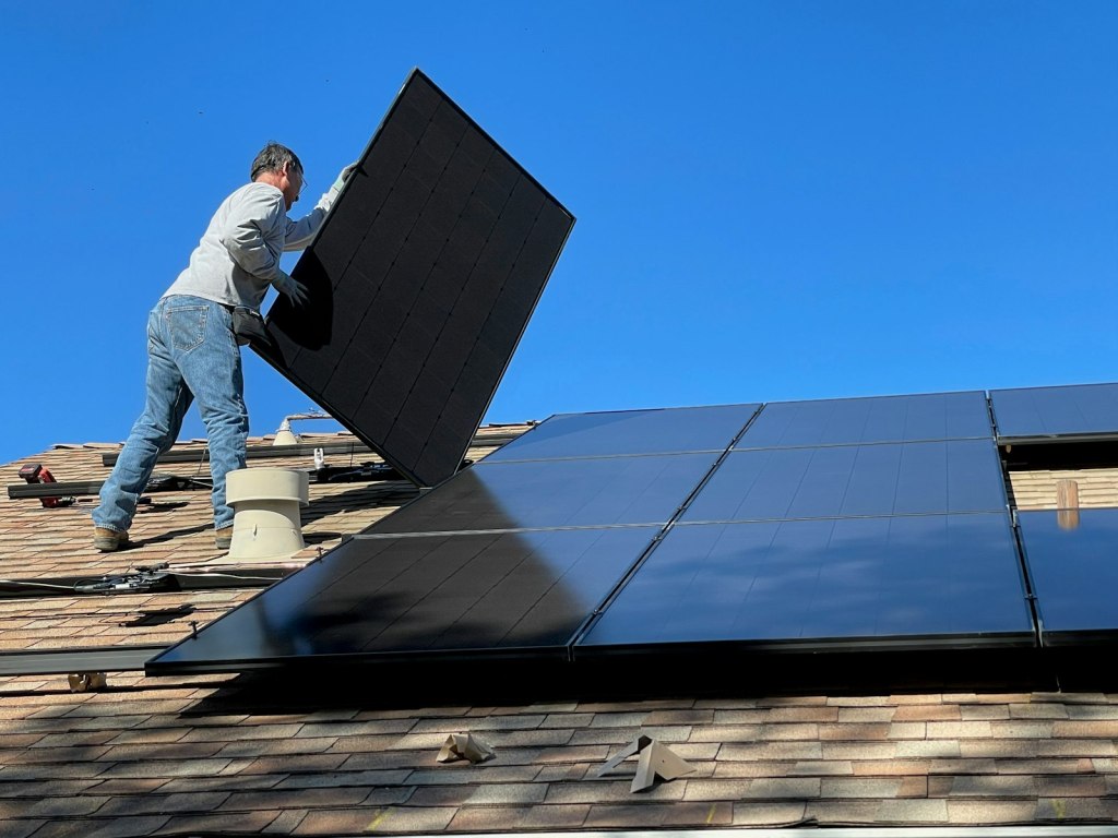 An installer fitting a solar panel on a house roof under blue sky