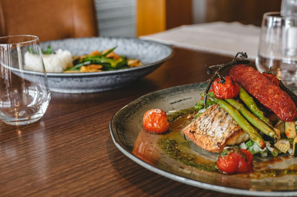 A plated restaurant dish of fish, tomatoes and greens on a wooden table
