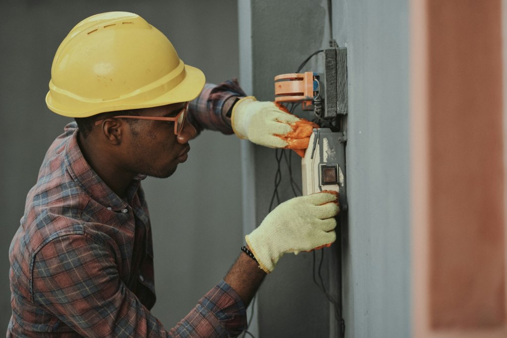 An electrician in a hard hat and gloves working on wiring